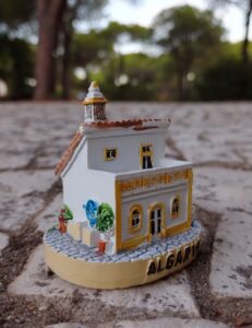 Uma miniatura de uma casa portuguesa do Algarve sobre calçada-mosaico e pinheiros ao fundo. Foto: ViniRoger