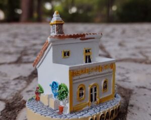 Uma miniatura de uma casa portuguesa do Algarve sobre calçada-mosaico e pinheiros ao fundo. Foto: ViniRoger