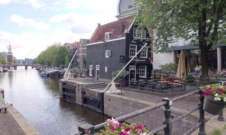 De Sluyswacht (bar em antiga torre do canal que entortou bastante com os anos) e canal Oudeschans com Montelbaanstoren ao fundo (torre de defesa do século 16, outrora parte das muralhas da cidade, com sinos e um relógio adicionado em 1606). Foto: ViniRoger