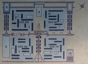Placa local com mapa da unidade de vizinhança que contém a SQS 308: superquadras residenciais (1), comércio local (2), igreja (3), escola parque (4), clube de vizinhança (5), posto de saúde (6), jardim de infância (7), biblioteca (8) e cinema (9).