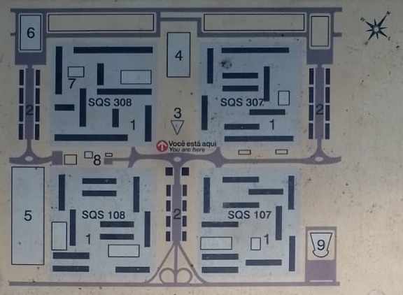 Placa local com mapa da unidade de vizinhança que contém a SQS 308: superquadras residenciais (1), comércio local (2), igreja (3), escola parque (4), clube de vizinhança (5), posto de saúde (6), jardim de infância (7), biblioteca (8) e cinema (9).
